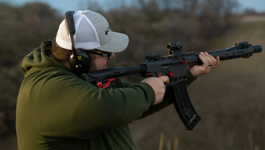Man holding a rifle that has a red dot sight mounted on it