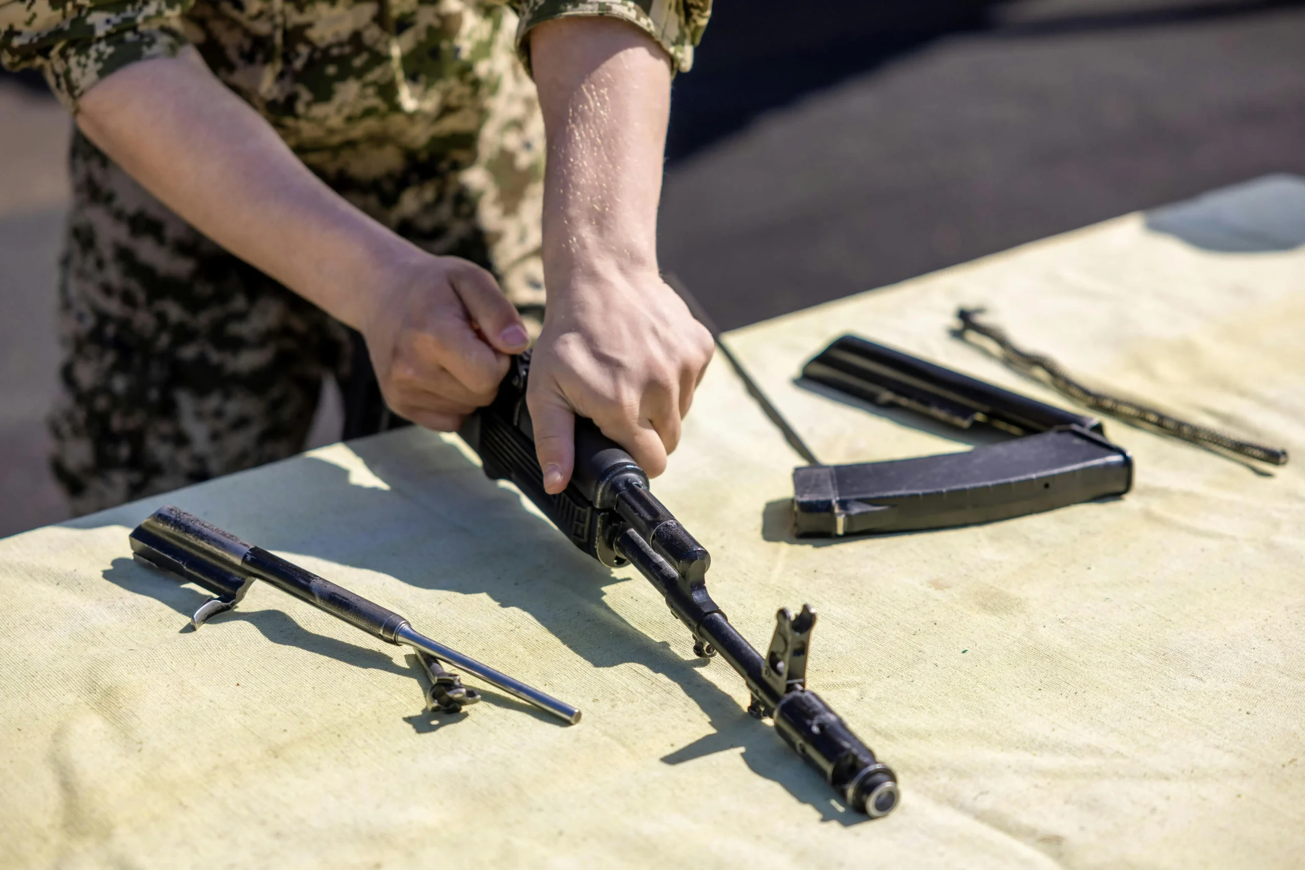 soldier or man assembling or disassembling a rifle, with some parts of it at the side of the table